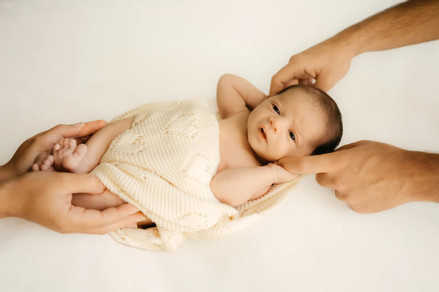 Bebé descansando sobre una manta con las manos de sus padres
